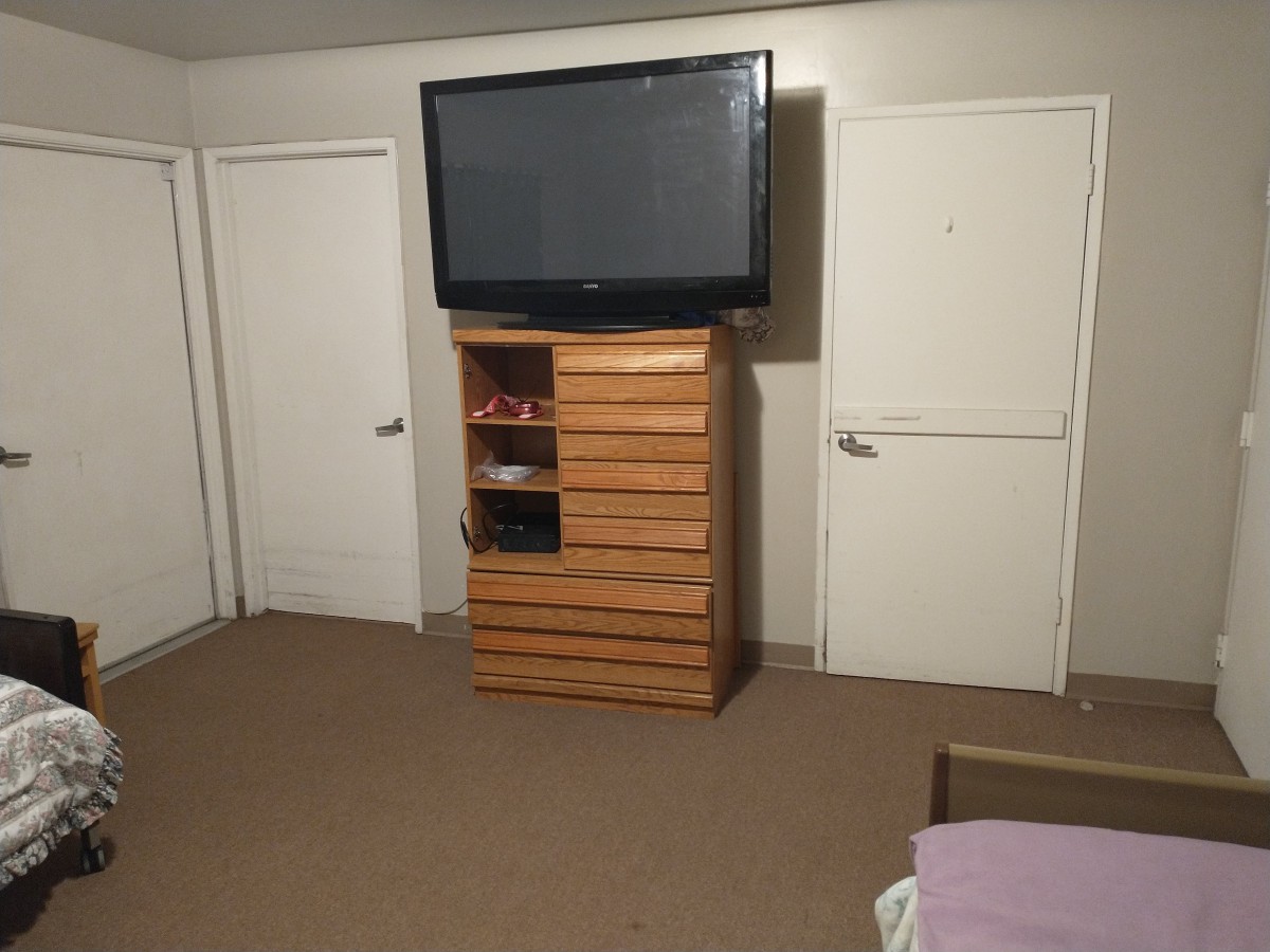 A minimalist room with a television on a dresser, flanked by two doors.