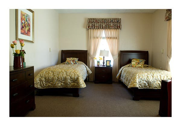 A bedroom with two twin beds and matching bedding, featuring a nightstand between them and a window with curtains.