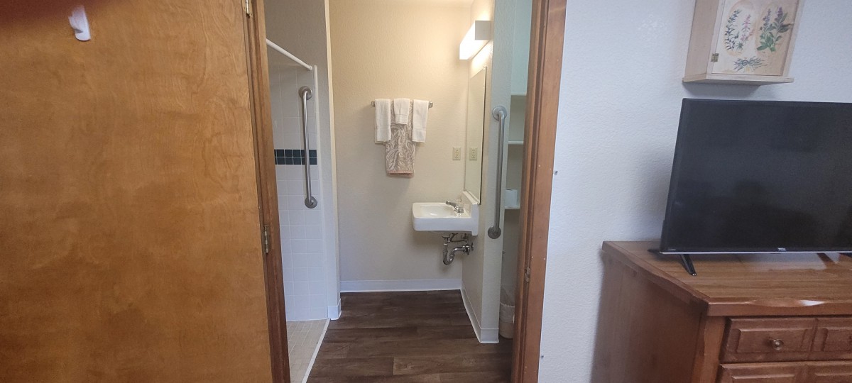 An accessible bathroom featuring a sink with handrails, towels, and a shower area.