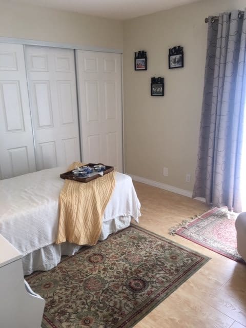A cozy bedroom featuring a neatly made bed with a decorative tray, carpet, and ample natural light.