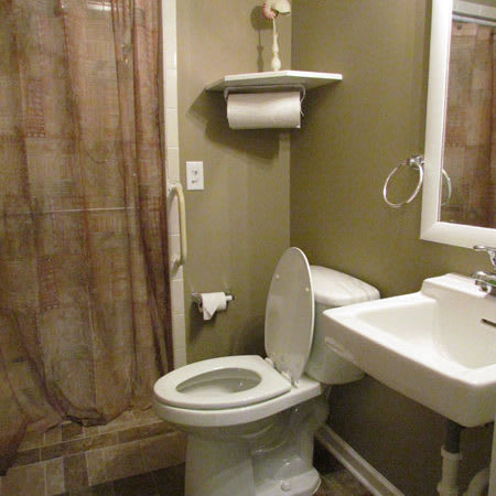 A small bathroom featuring a toilet, sink, mirror, and shower with a brown curtain.