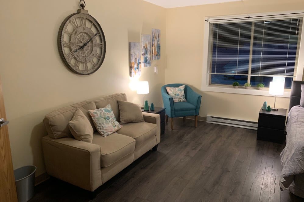 A cozy living room with a beige sofa, decorative clock, and a teal chair.