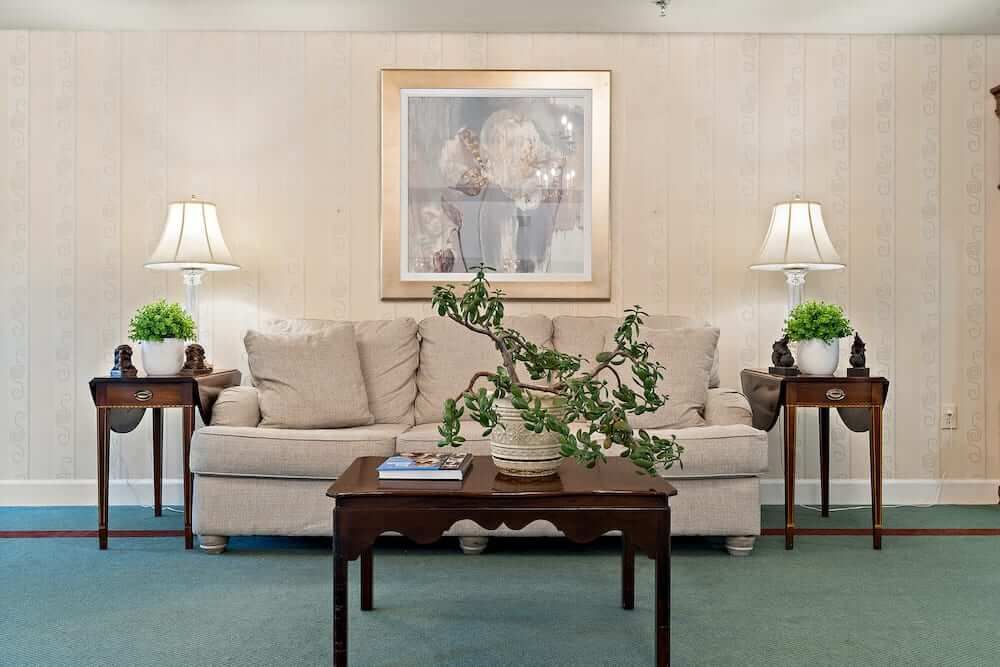 A cozy living room with a sofa, coffee table, and decorative plants, featuring a framed painting on the wall.