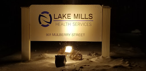 Sign for Lake Mills Health Services located at 901 Mulberry Street, illuminated at night.