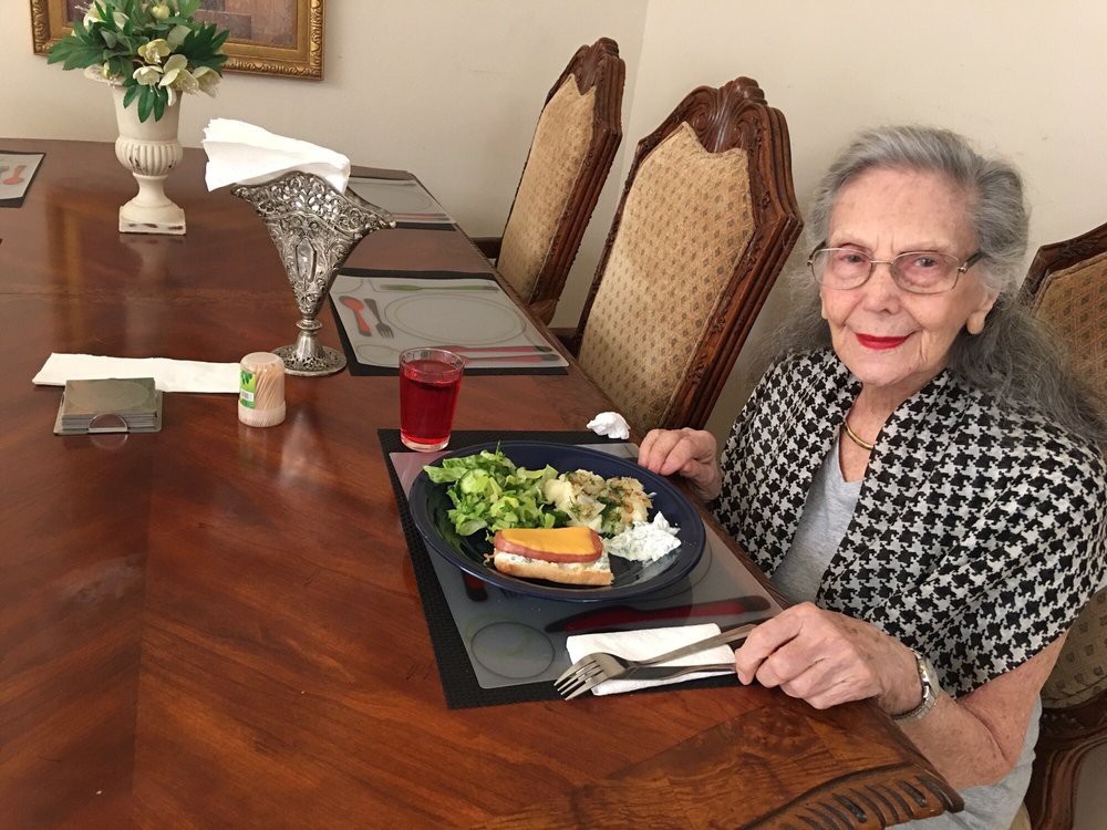 An elderly woman enjoying a meal at a dining table.