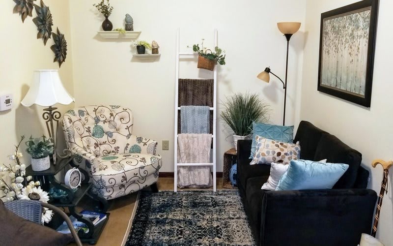 A cozy living room with a patterned armchair, dark sofa, decorative ladder, and floor lamp.