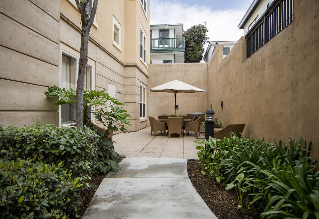 A cozy courtyard with patio furniture and an umbrella, surrounded by plants and urban architecture.