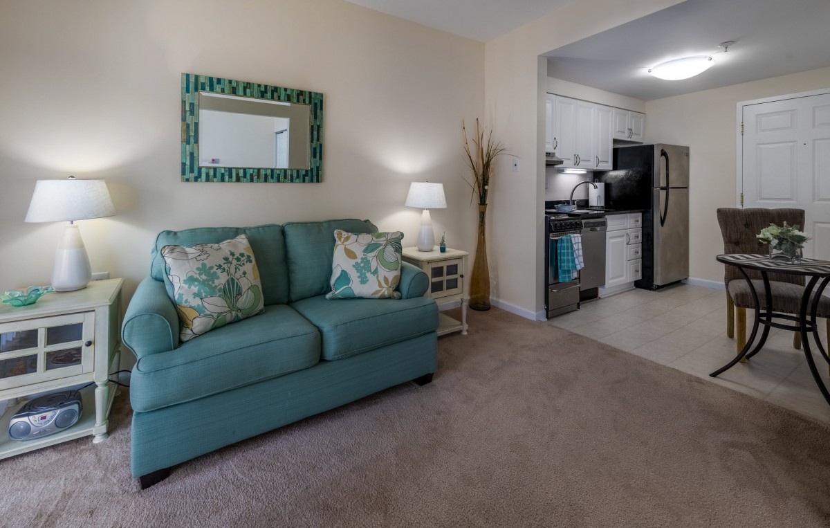 A cozy living room with a teal sofa and an adjoining kitchen.