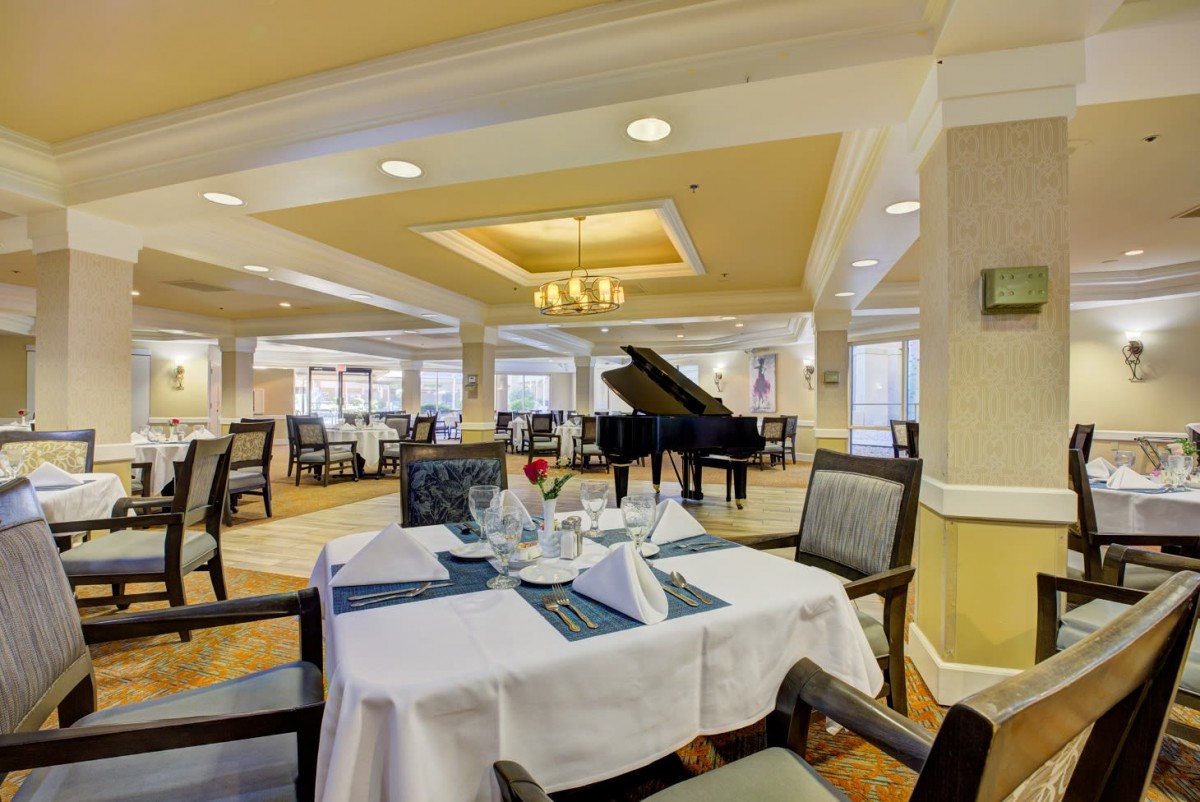 An elegant dining room with a grand piano and neatly set tables.