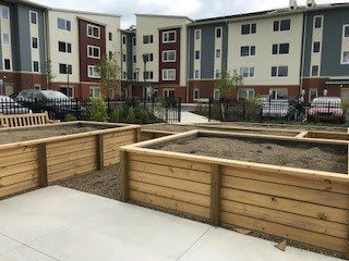 A view of an apartment complex with wooden raised garden beds in the foreground, showcasing urban gardening opportunities.