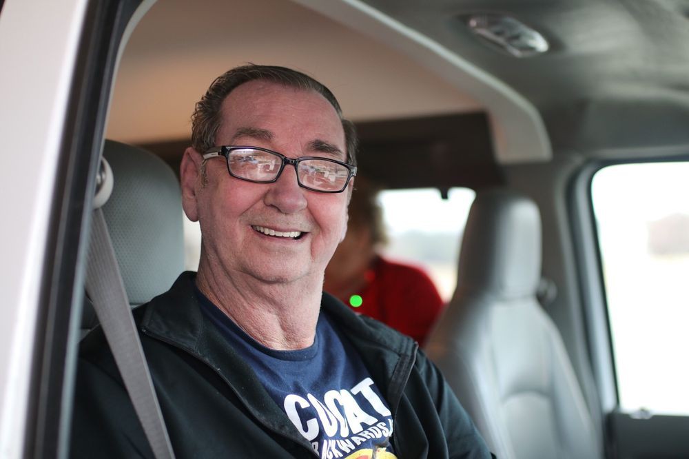 A smiling man wearing glasses is sitting inside a vehicle.
