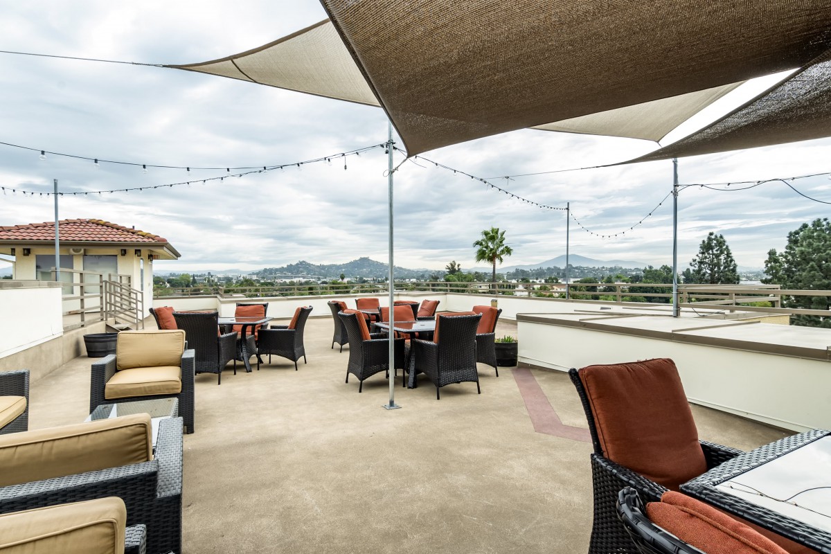 An outdoor patio with tables and chairs, shaded by sail canopies, offering a scenic mountain view.