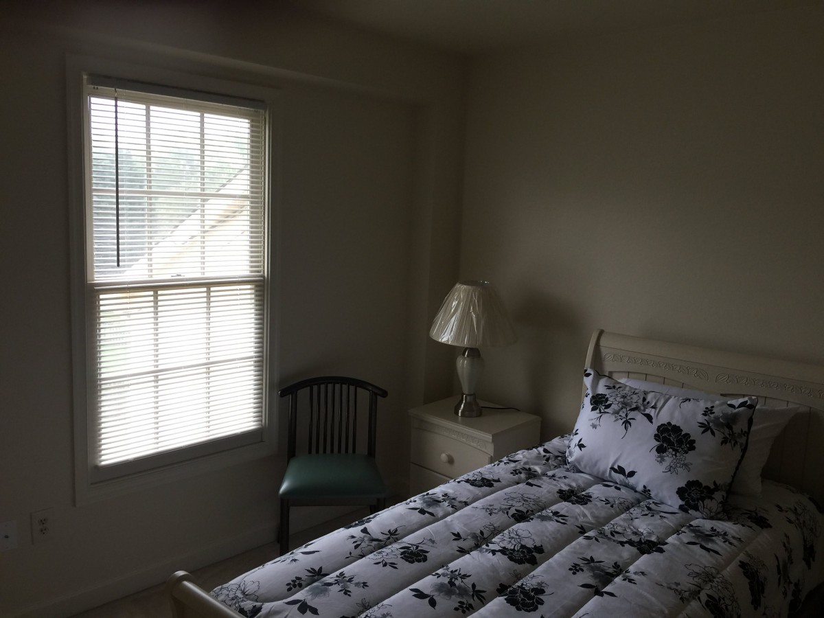 A cozy bedroom with a bed, a lamp on a side table, and a window letting in natural light.