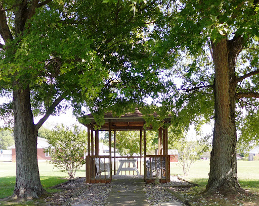 A serene gazebo nestled between two lush trees in a peaceful park setting.