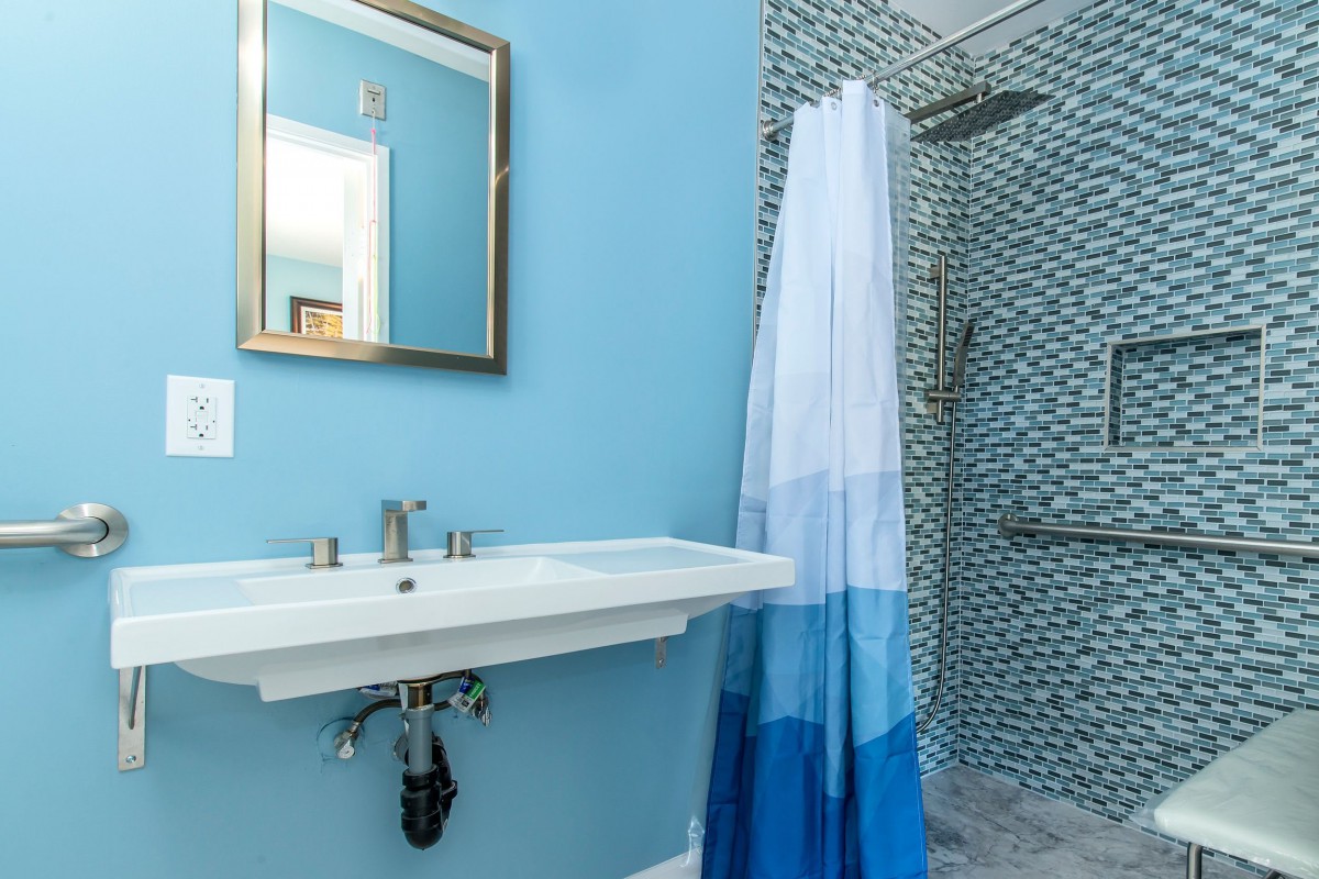 A modern bathroom with blue walls, featuring a sink, mirror, and tiled shower area.