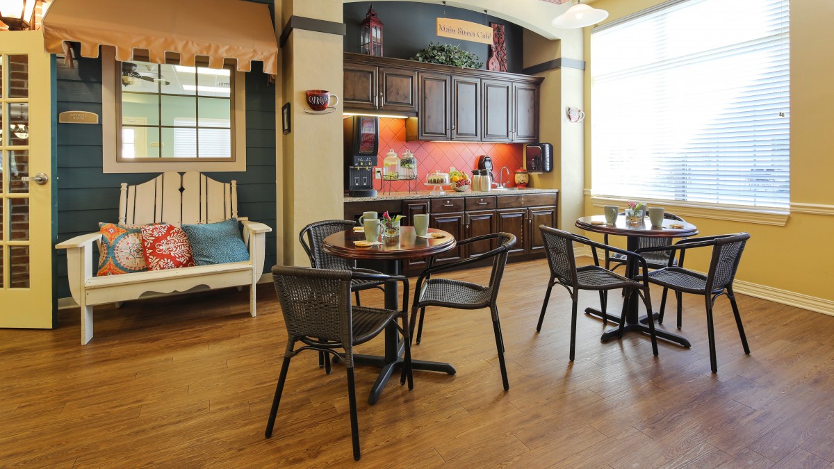 A cozy kitchen and dining area with wooden flooring, featuring tables and chairs under natural light.