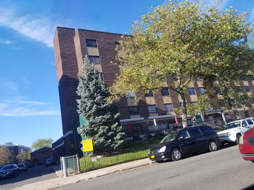 A view of a multi-story apartment building surrounded by trees and parked cars under a clear blue sky.