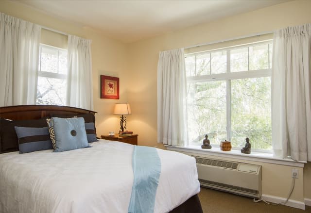 A cozy bedroom with a large window, a neatly made bed, and soft lighting.