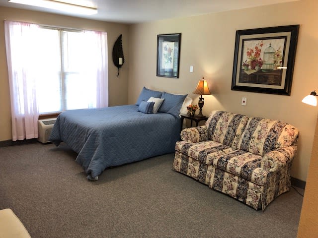 A cozy bedroom with a blue bedspread, floral couch, and decorative artwork on the walls.