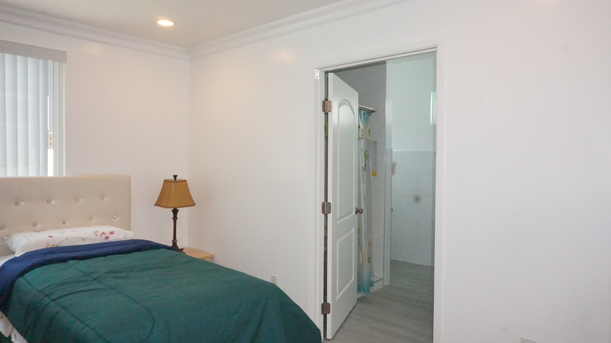 A bedroom with a green bedspread, a bedside lamp, and an open doorway leading to a bathroom.