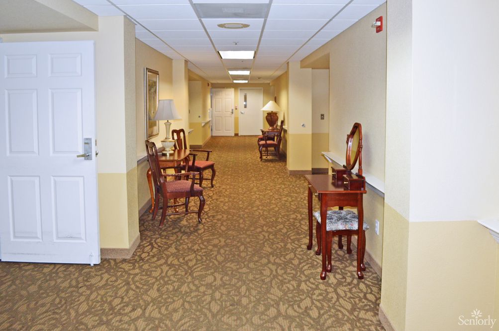 A carpeted hallway with chairs and tables, featuring decorative lighting.
