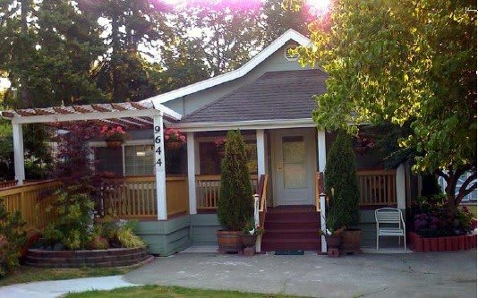 A charming house with a front porch surrounded by trees and greenery in the daytime.