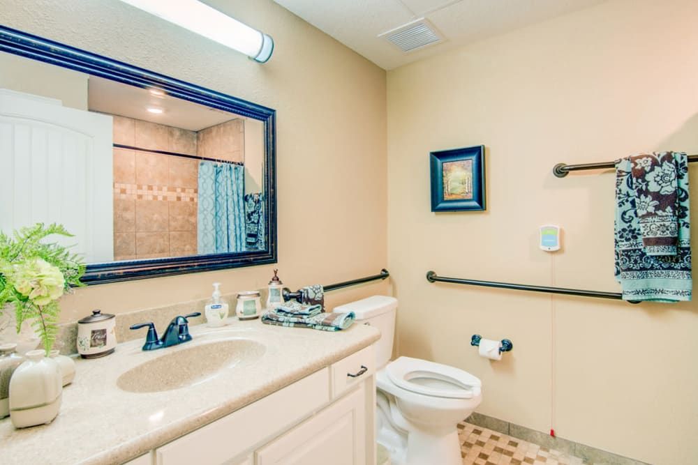 A well-lit bathroom featuring a sink, mirror, toilet, and bathtub with a patterned tile floor.