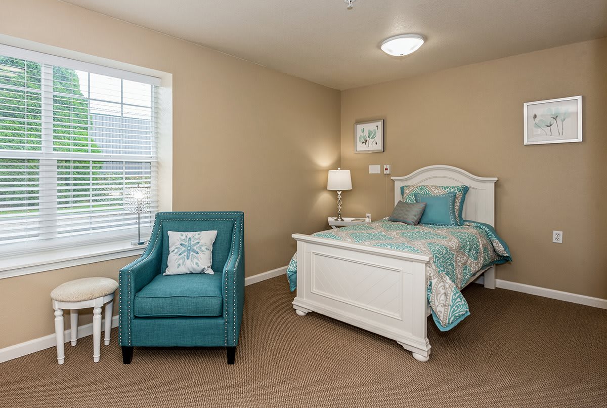 A cozy bedroom with a white bed and teal accents, featuring an armchair and soft lighting.