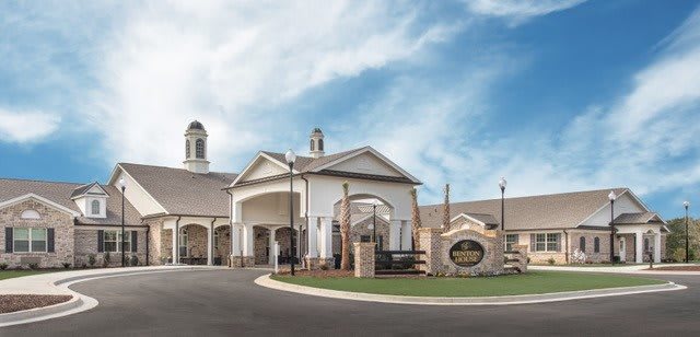 A large building with an arched entrance and a circular driveway under a partly cloudy sky.