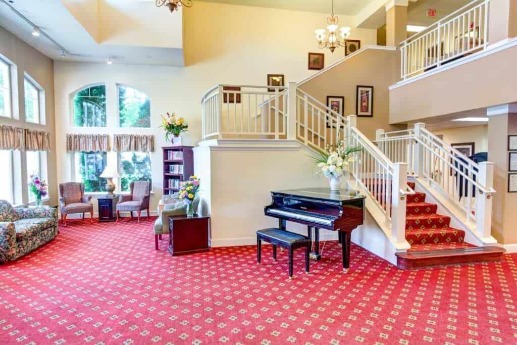 A spacious lobby featuring a grand piano, carpeted flooring, and a staircase leading to the upper level.