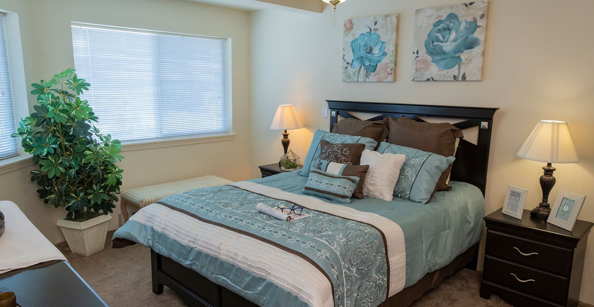 A well-decorated bedroom with a neatly made bed, artwork on the wall, and a lamp on the nightstand.