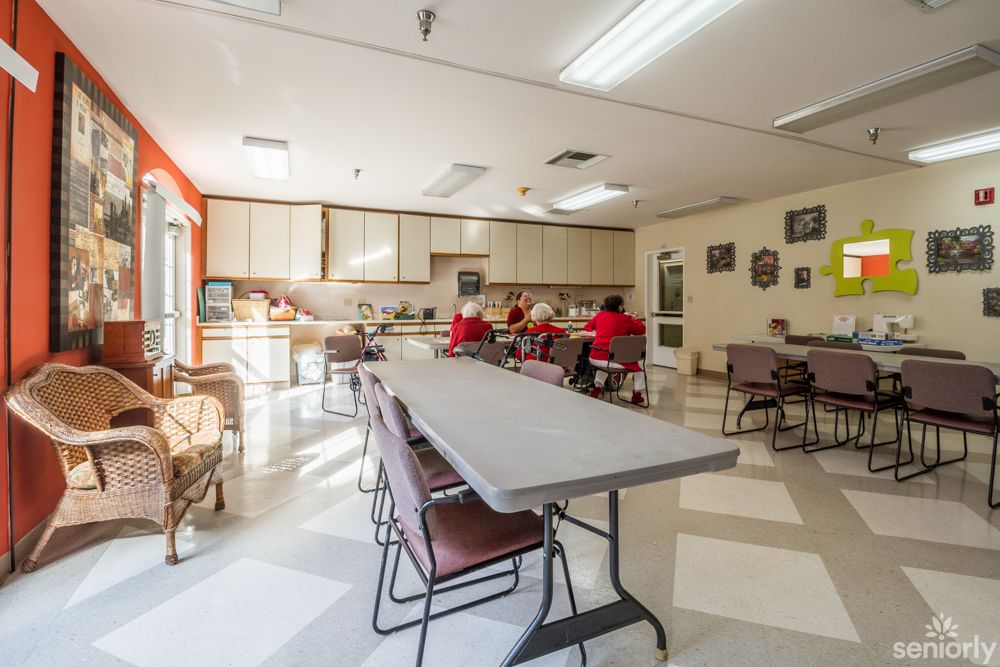 A community dining area with tables, chairs, and a kitchen in the background.