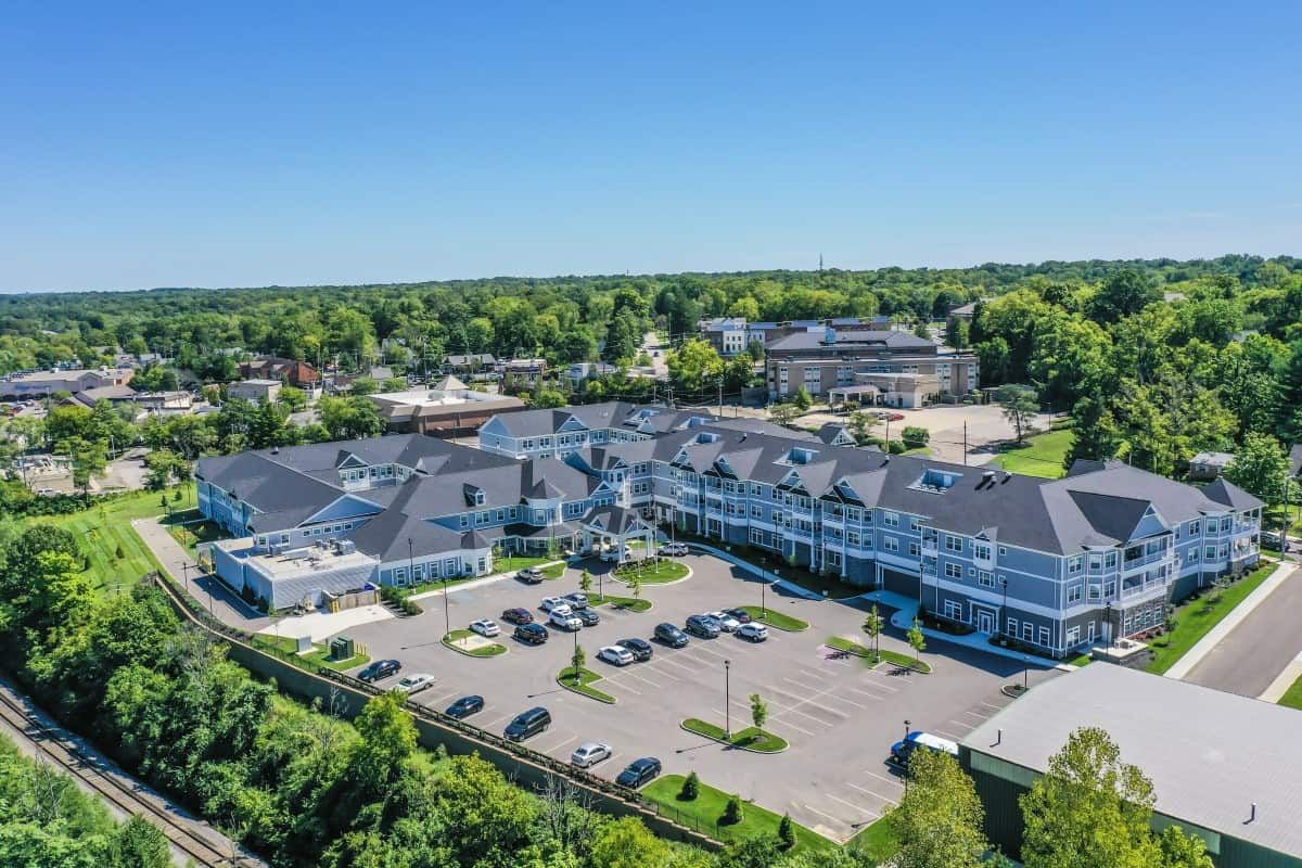 Aerial view of a modern building complex with a parking lot surrounded by trees on a sunny day.