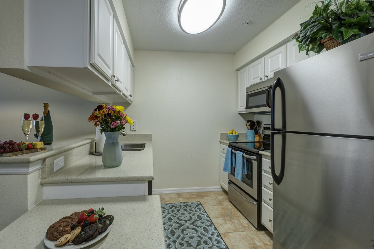 A modern kitchen with stainless steel appliances and white cabinets, featuring a decorative rug and flowers on the counter.