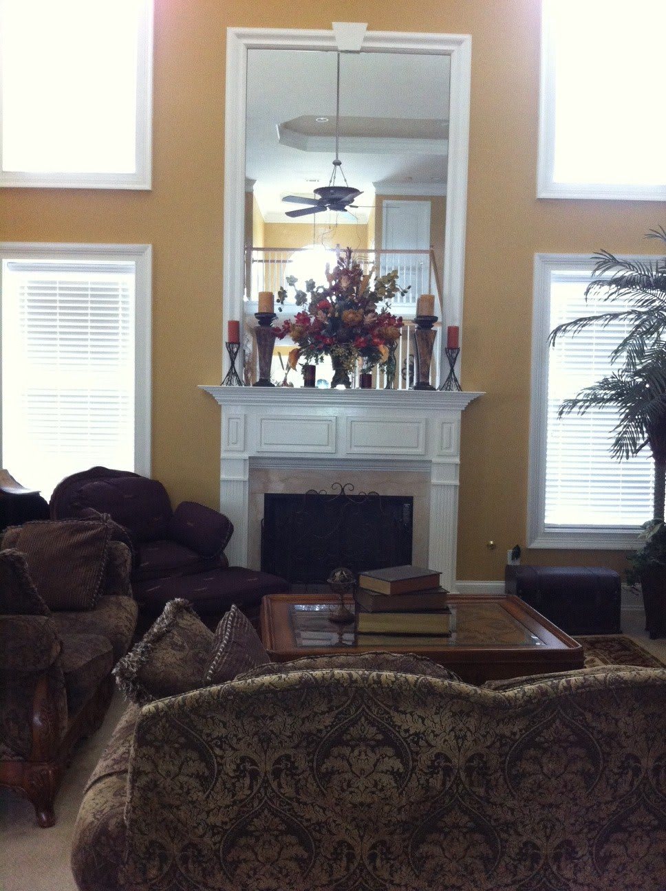 A cozy living room with a fireplace, surrounded by sofas and a coffee table, adorned with decorative items and large windows.