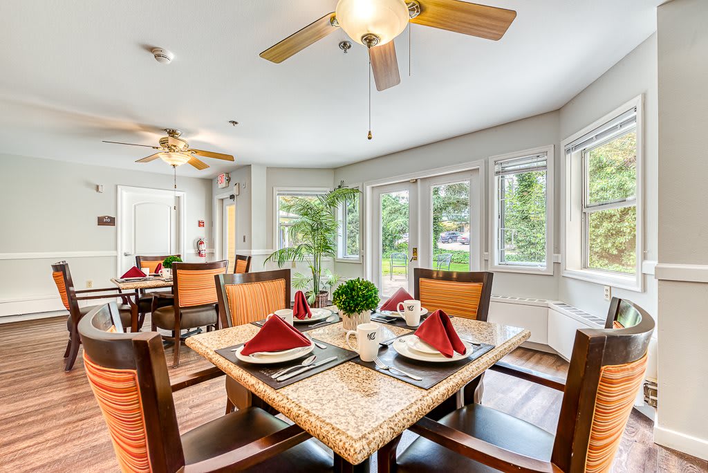 A spacious dining room with a well-set table, featuring red napkins and surrounded by large windows and natural light.