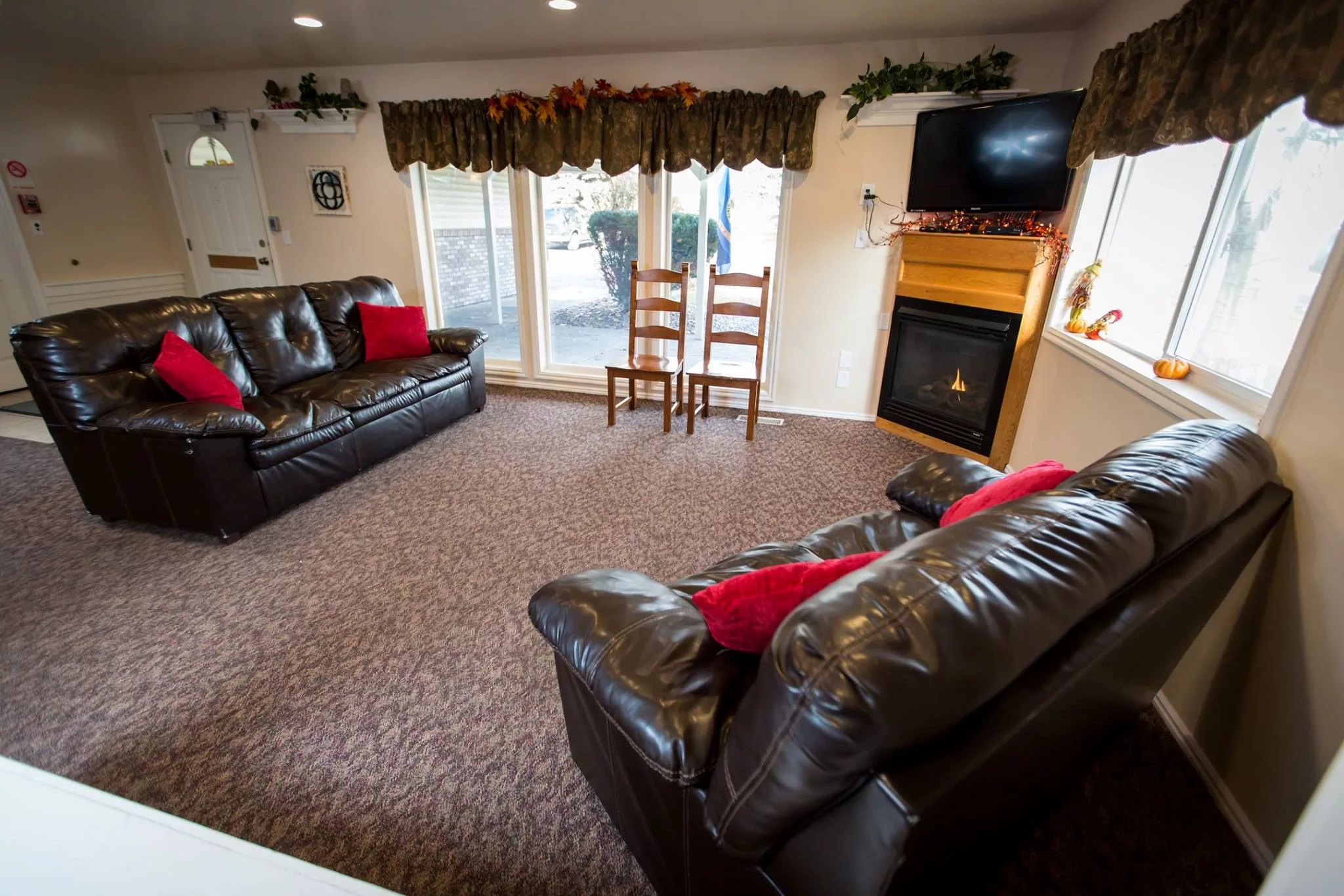 A cozy living room featuring leather sofas, a television above a fireplace, and large windows with drapes.