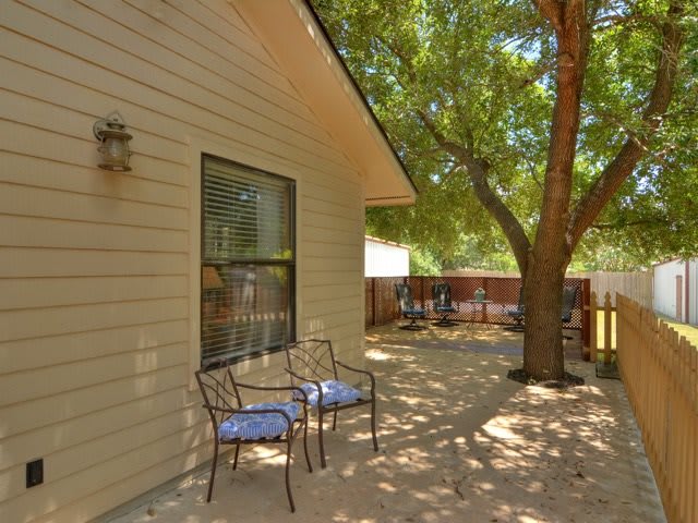 A peaceful backyard patio with chairs under the shade of a tree.