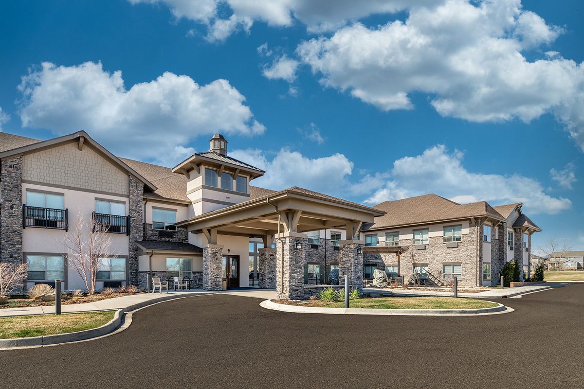 A modern residential building with a covered entrance and a spacious driveway under a partly cloudy sky.