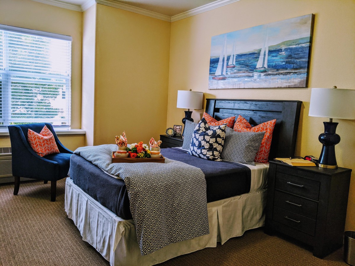 A cozy bedroom with a neatly made bed, decorative cushions, and nautical-themed artwork above the headboard.