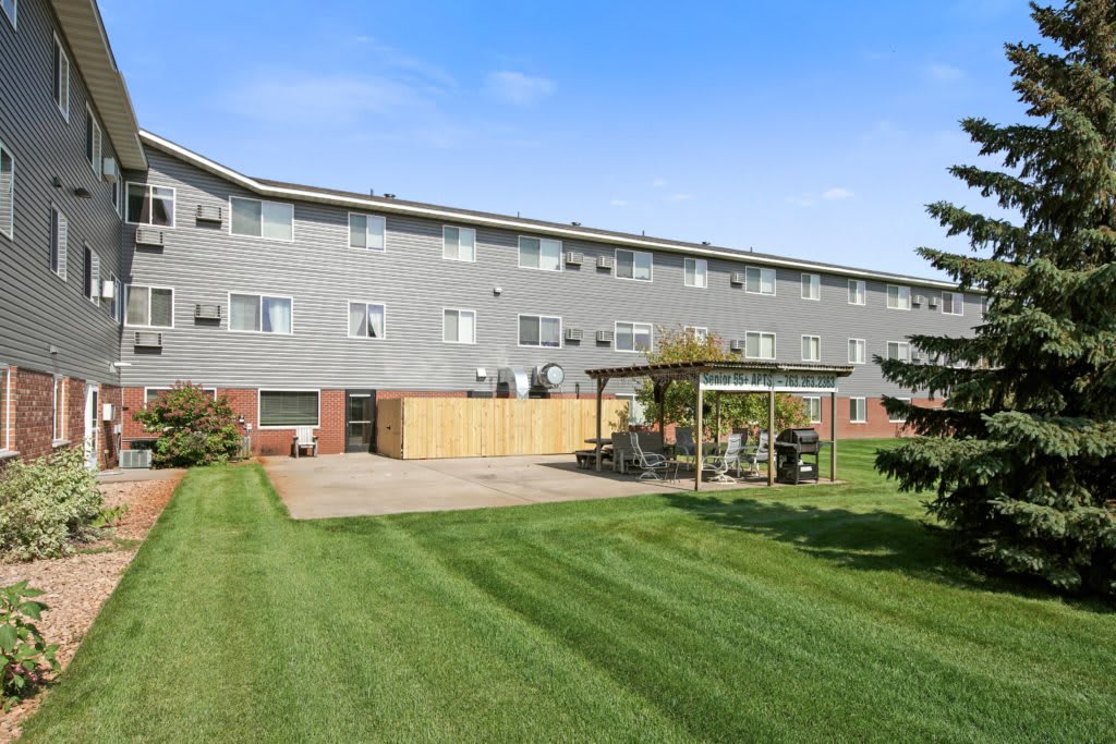 A view of an apartment building with a well-maintained lawn and patio under a clear blue sky.