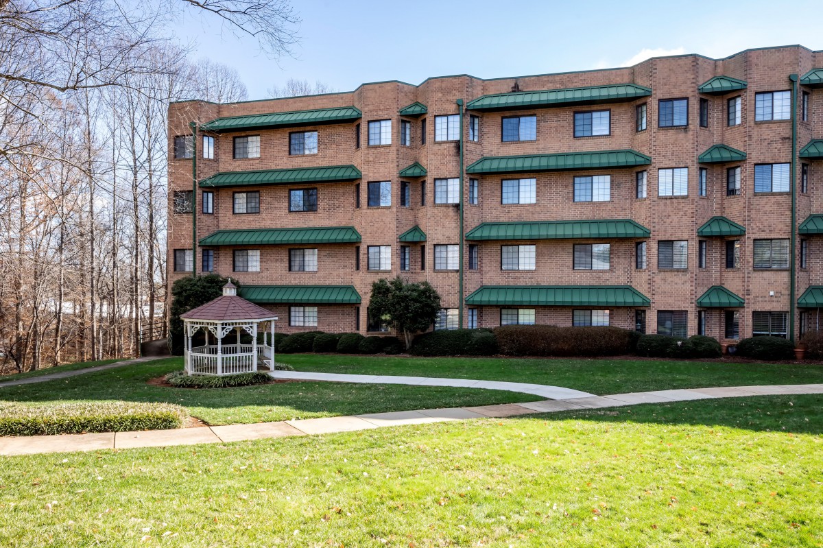 A residential apartment building with multiple balconies, a well-maintained lawn, and a gazebo in the foreground.