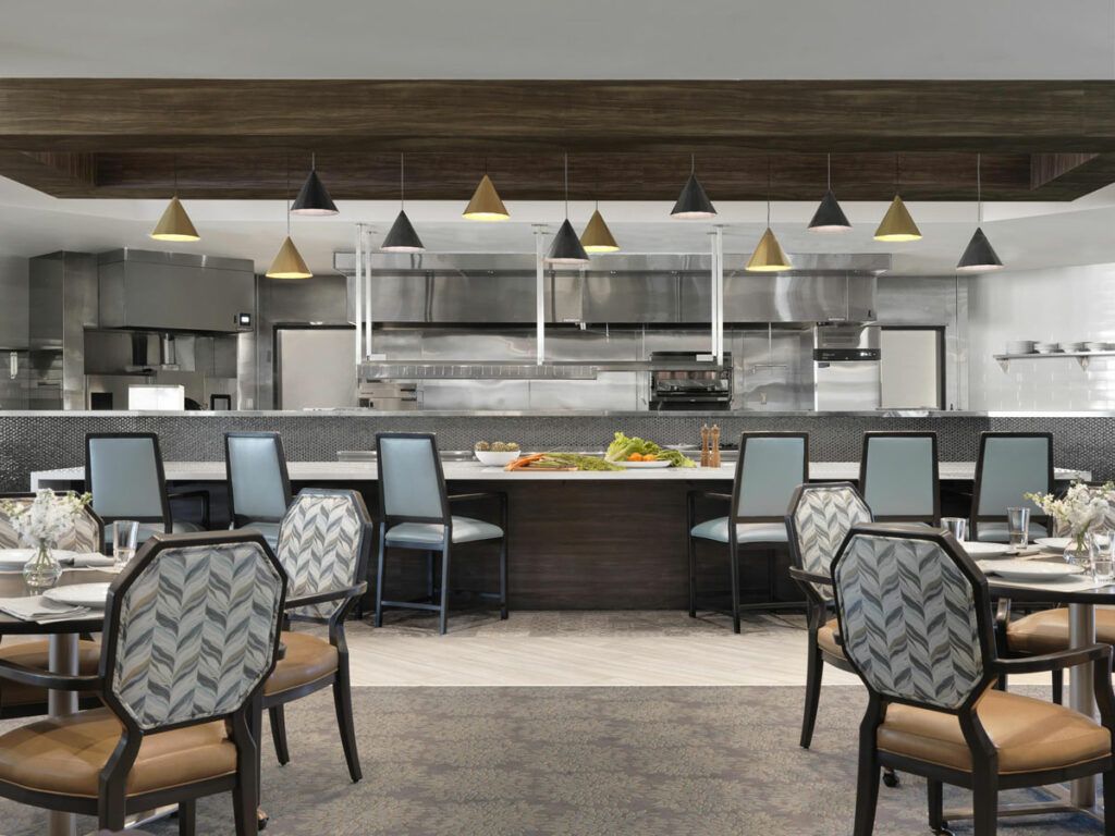 Modern restaurant interior featuring a dining area with patterned chairs and an open kitchen.