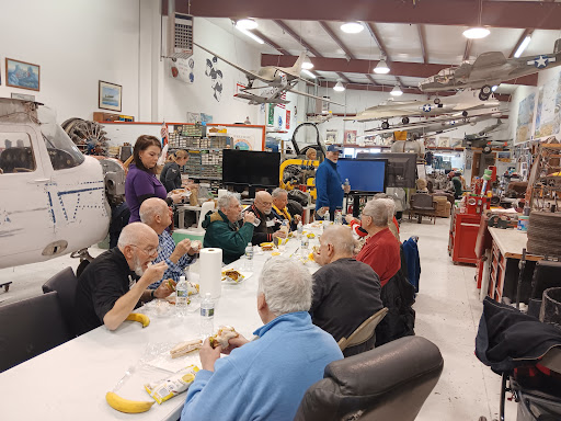 A community gathering of elderly individuals enjoying a meal together in an aviation-themed indoor space.