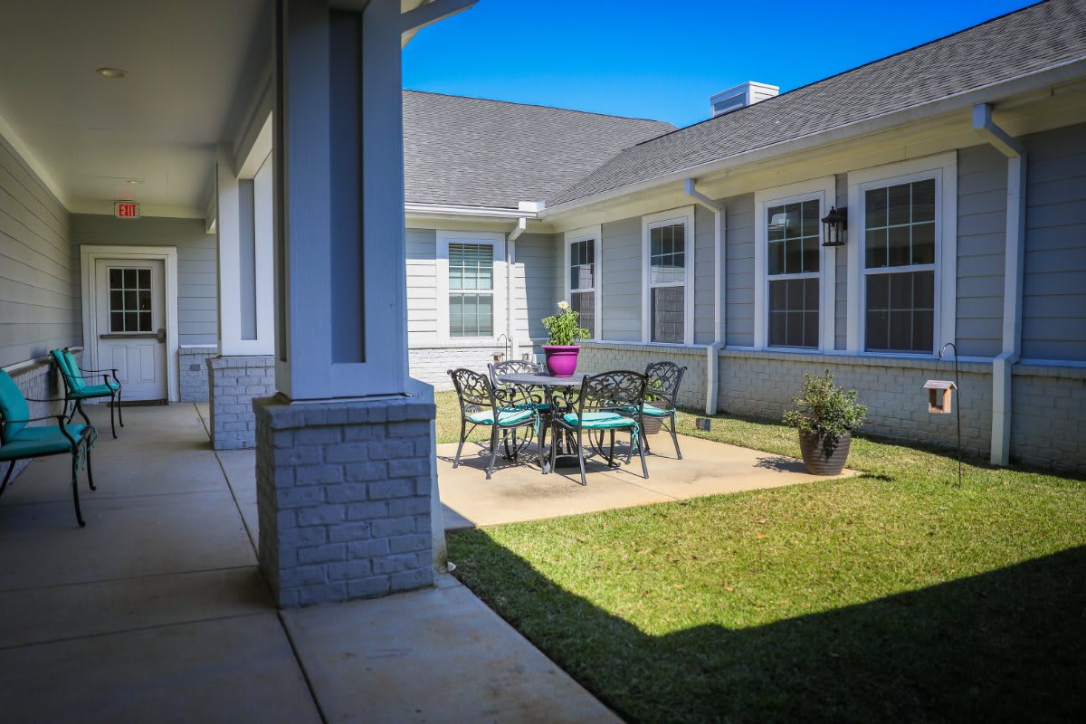 A cozy outdoor patio area with a round table and chairs, surrounded by a well-maintained lawn in a courtyard setting.