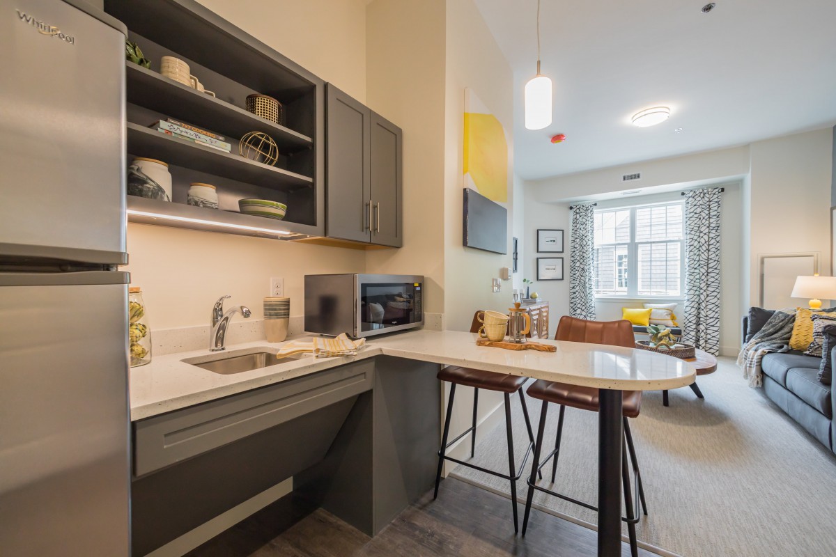 A modern kitchen and dining area in an apartment, featuring a countertop with stools, a microwave, and open shelving.