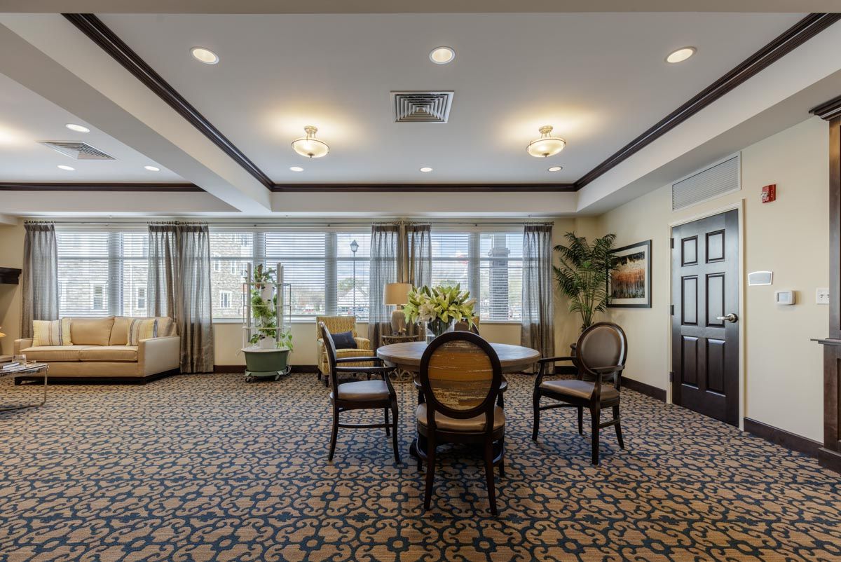 A spacious and elegant dining room with a central table, surrounded by chairs and large windows.