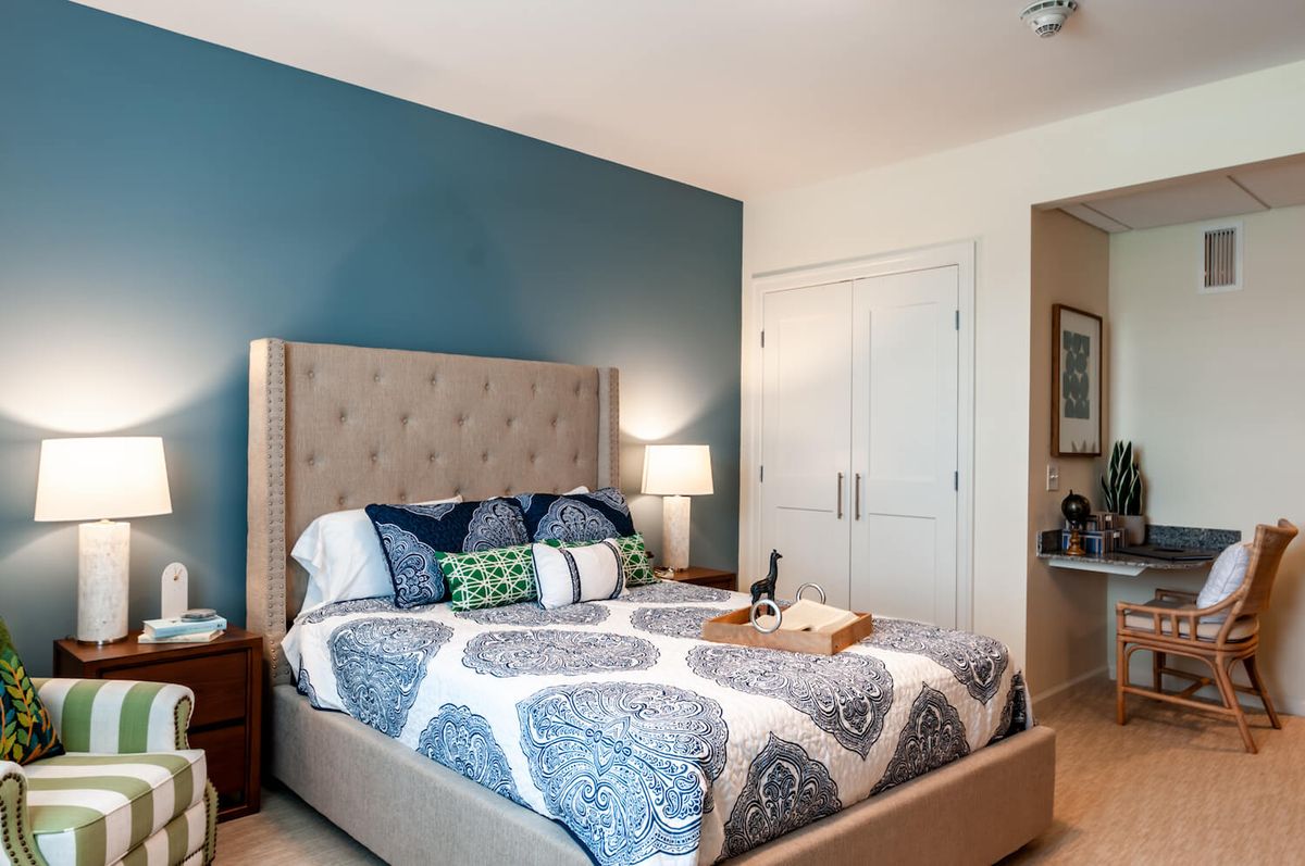 A modern bedroom with a blue accent wall, featuring a cozy bed adorned with decorative pillows and a bedside lamp.