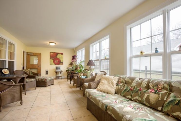 A bright and cozy living room with large windows, comfortable seating, and lush indoor plants.
