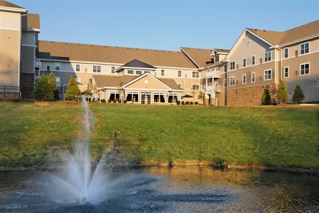 A large building with multiple gables and a scenic pond featuring a fountain in front.